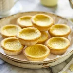 Baby lemon impossible pies on a rustic plate with golden tops, served on a marble counter with tea set nearby