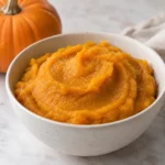 Bowl of smooth homemade pumpkin puree with a small sugar pumpkin in the background
