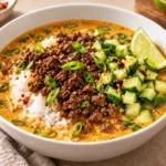 Beef broth bowl with browned ground beef, jasmine rice, coconut curry broth, cucumber, green onions, sesame seeds, and lime