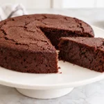 Round black bean chocolate cake with a slice cut out, showing its dense chocolate crumb