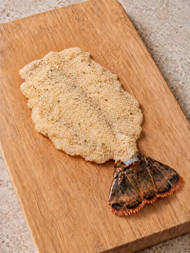 Raw lobster tail cutlet coated in fine seasoned breadcrumbs with the tail fin attached
