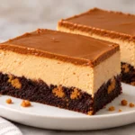 Two slices of brownie bottom Biscoff cheesecake with creamy filling and smooth cookie butter topping on a white plate
