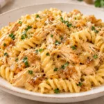 Creamy caramelized onion chicken pasta with fusilli, shredded chicken, Parmesan, and parsley served on a white plate.