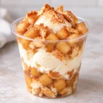 Homemade apple pie sundae in a clear cup with vanilla ice cream, cinnamon apples, and crispy pie crust pieces.