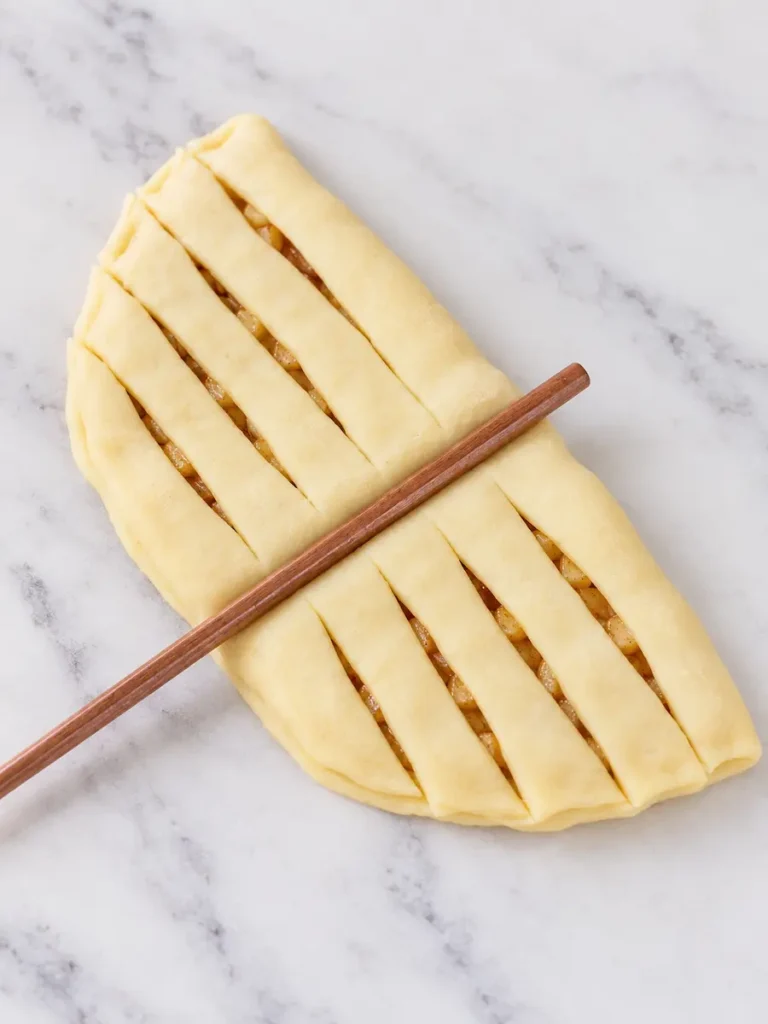 Folded apple-filled dough cut into strips on both sides of a wooden guide for twisted apple pie rolls