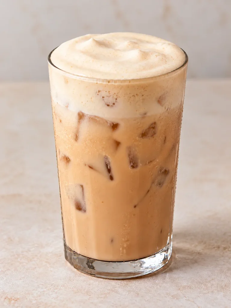 Iced banana bread chai in a clear glass topped with creamy brown sugar cold foam before adding cinnamon sugar.
